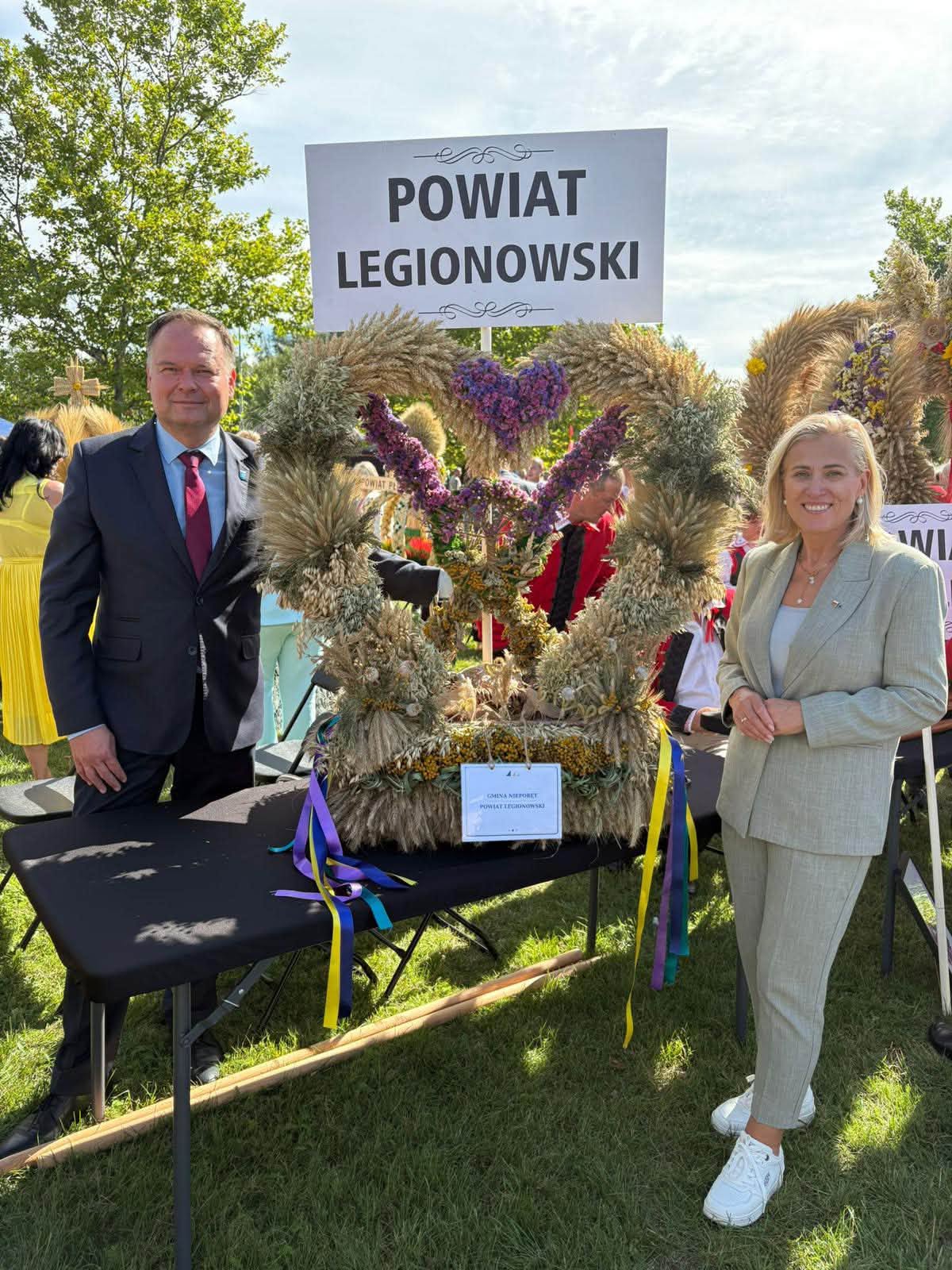 zdjęcie przedstawiające dwie osoby z wieńcem dozynkowym i tablicą Powiat Legionowski